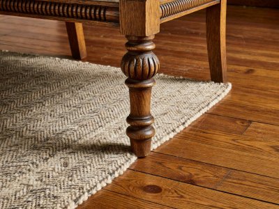 Close-up of a turned oak armchair leg resting six inches onto a woven wool rug over hardwood flooring